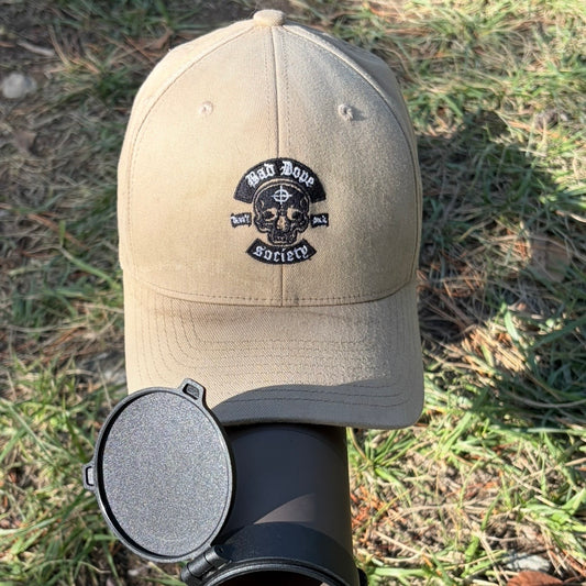 Bad Dope Society Flex Hat, khaki, front view with embroidered skull logo, resting on a riflescope