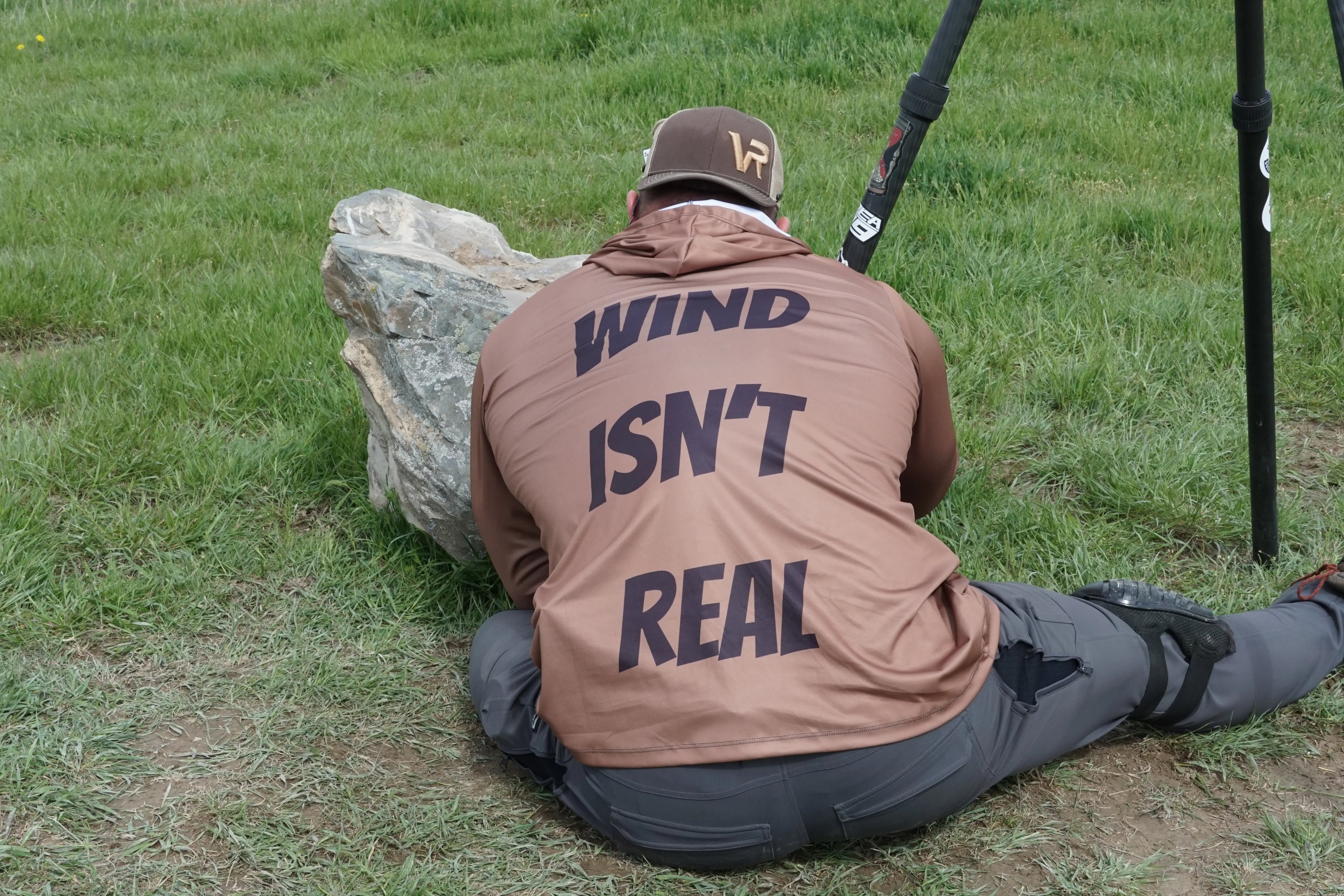 Bad Dope Society Wind Isn't Real Sun Shirt, tan, back view, sitting position behind a rock with a tripod